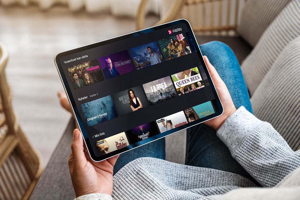 A person in front of the tv holding a tablet with the Viaplay app